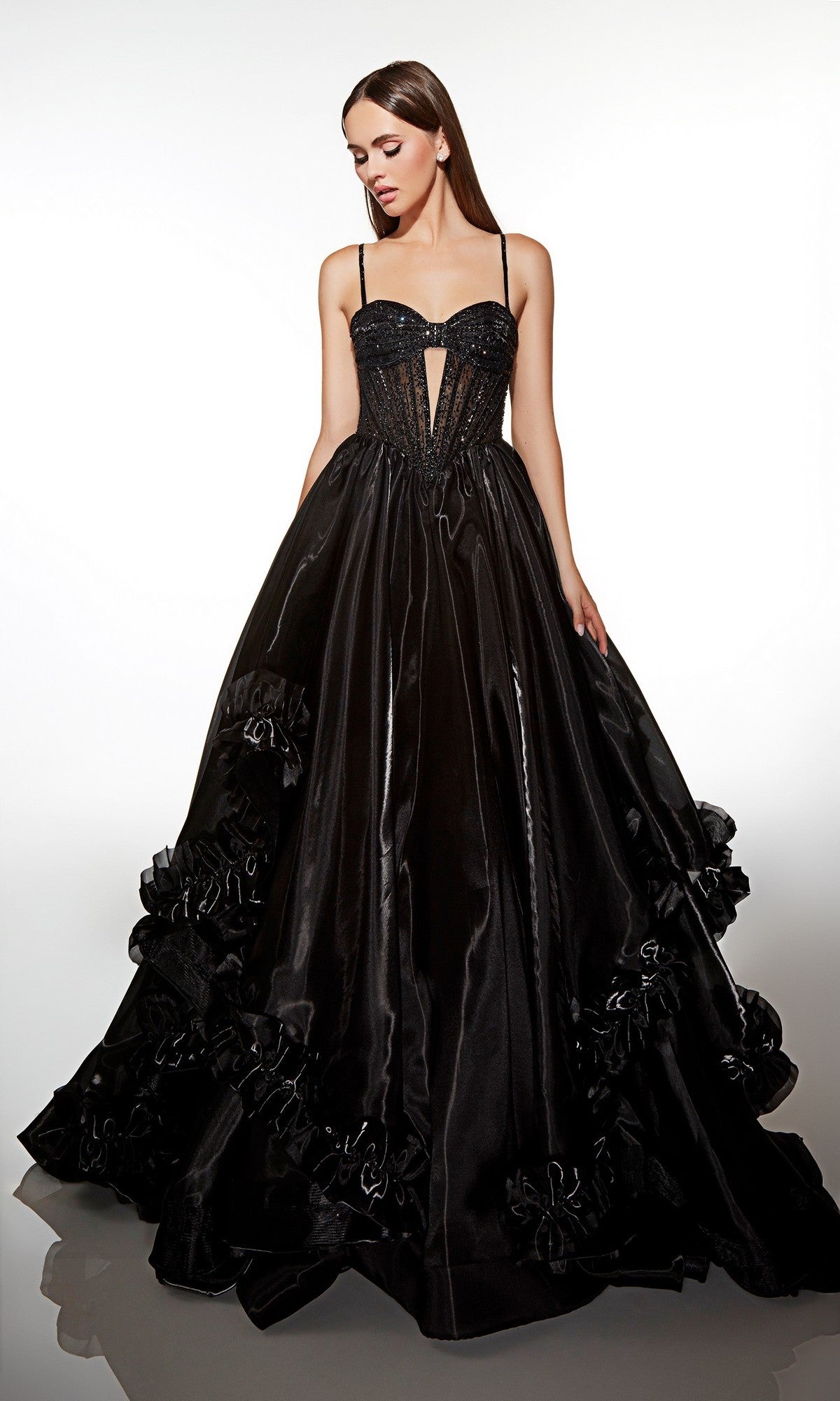 A woman stands wearing the Alyce 62107, a black, floor-length prom dress featuring a sleeveless corset bodice and a voluminous skirt with ruffled details.